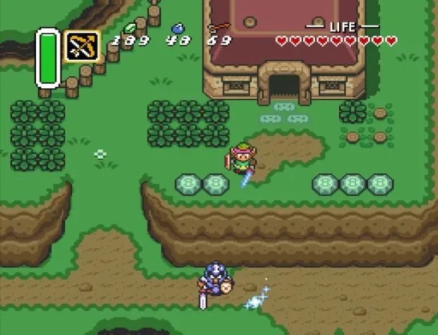 Link standing on a grass path outside a stone building, sword drawn, hearts and rupee counts along the top of the screen.